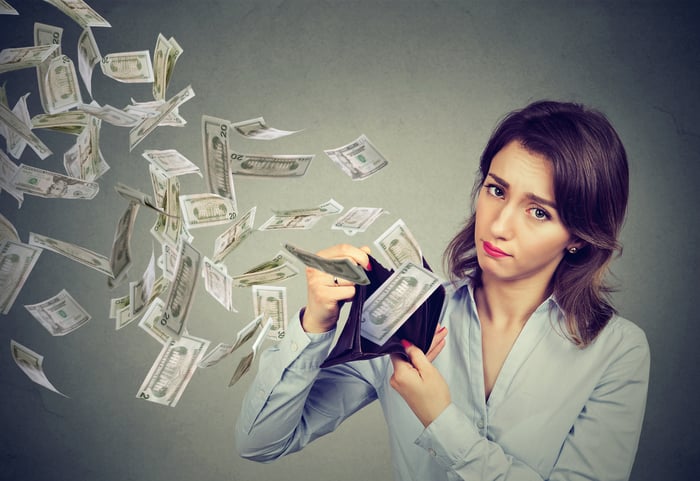 Woman holding a wallet open with numerous bills flying out of it