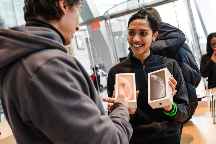 Woman in Apple store, holding up two iPhone boxes and smiling