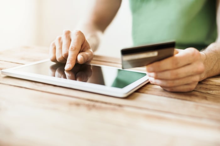 A man interacting with a tablet computer with one hand while the other hand holds a credit card.