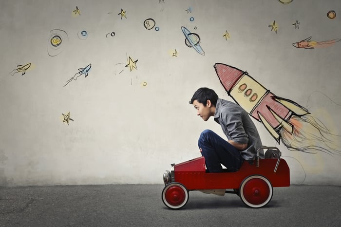 A man in a toy car with a rocket ship drawn on a wall behind him.