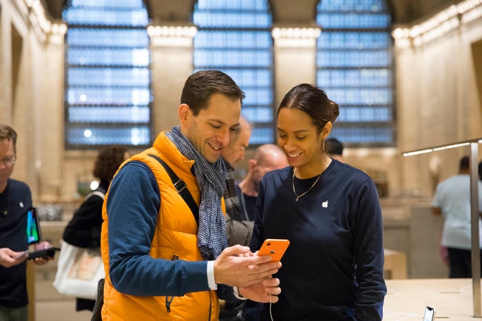 A man and an Apple employee looking at an orange iPhone XR.