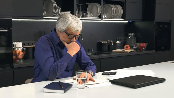 Senior man looking at documents while seated at his kitchen table.