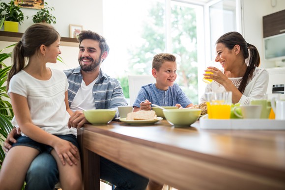 Man, woman, young boy, and young girl at table with bowls and plates in front of them