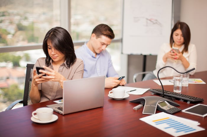 Man and two women checking phones at conference table