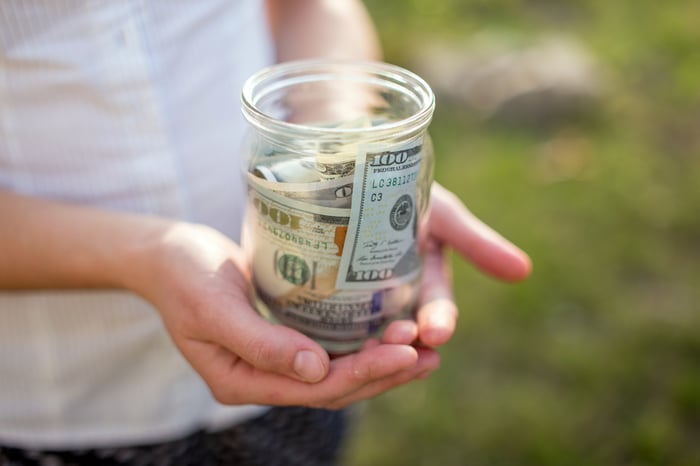 Woman holding jar filled with $100 bills