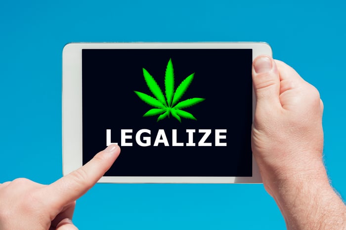 A person touching the screen of a tablet, with the word legalize and a cannabis leaf on the screen.