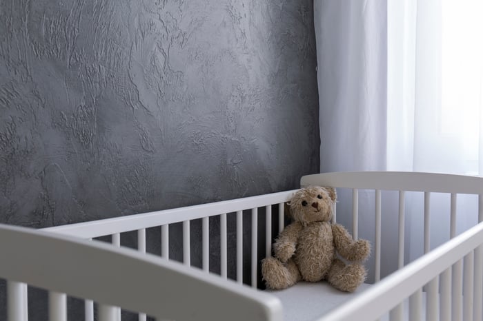 An empty baby crib with a stuffed animal in the corner. 