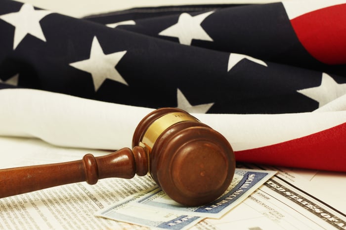 A judge's gavel lying atop two Social Security cards, with an American flag in the background.