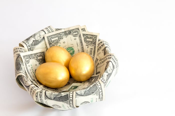 A basket covered in dollar bills that contains three golden eggs. 