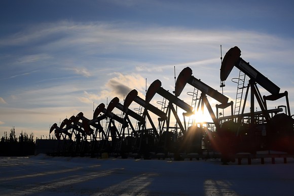 A long row of pumpjacks under the setting sun with snow in the foreground