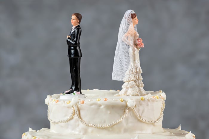 Bride and groom figurines facing away from each other on top of a wedding cake.