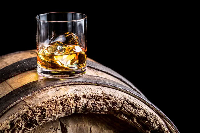 Rocks glass with whiskey and ice cubes in it sitting on a whiskey barrel