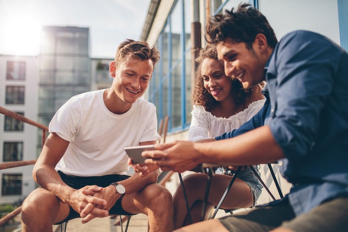 A young woman and two young men on a balcony watching a video on a smartphone