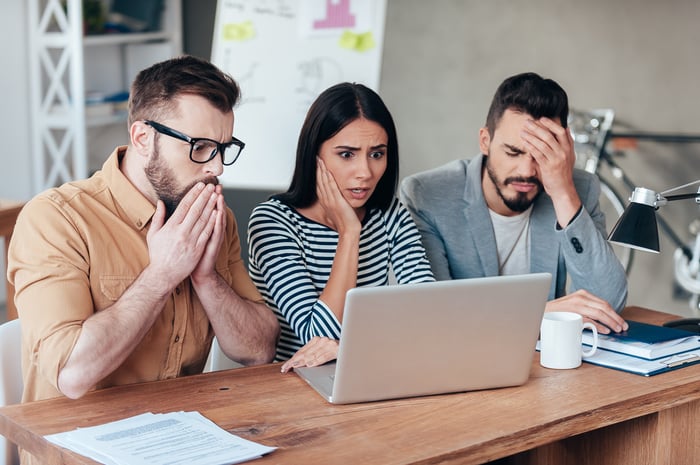 Three people looking at a computer screen and acting concerned.