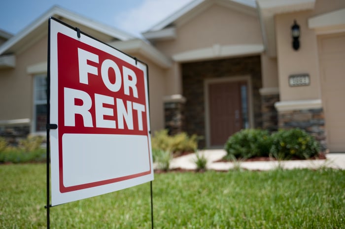 A "for rent" sign placed on the front lawn in front of a single-family home.