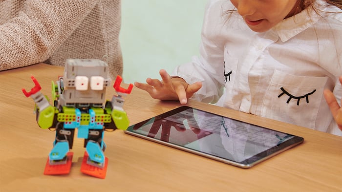 A girl using an iPad with a toy robot on the table.