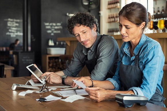 Man and woman looking through receipts with a tablet and calculator on the table where they're spread out
