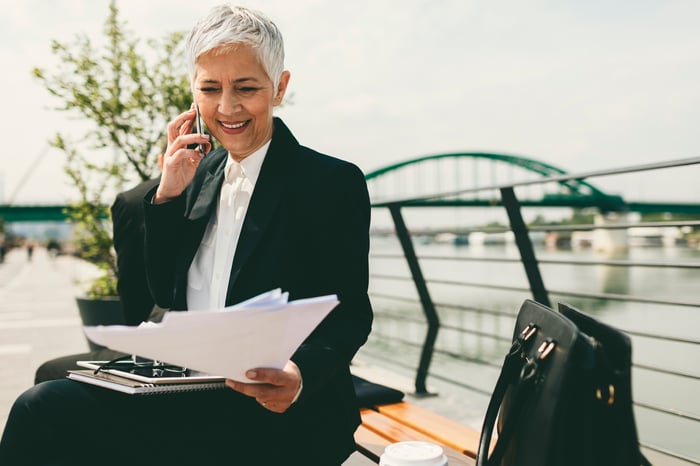 Mature businesswoman talking on the phone while looking at some paperwork on a bench outside