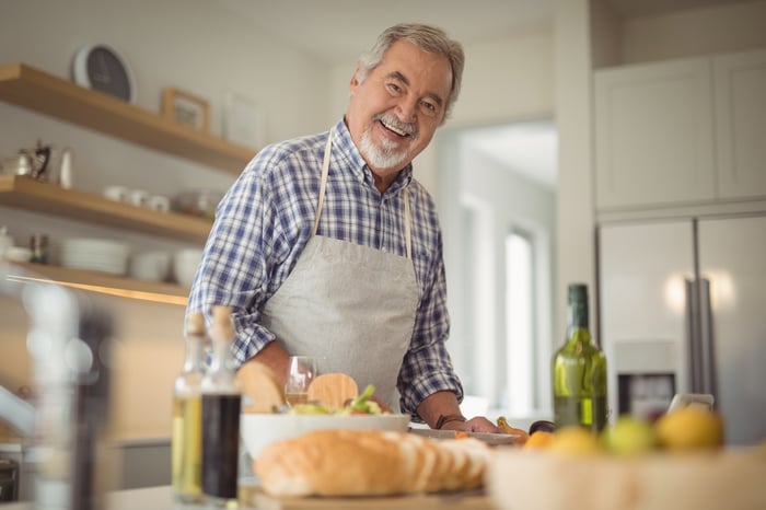 Smiling senior man in apron at a kitchen counter.