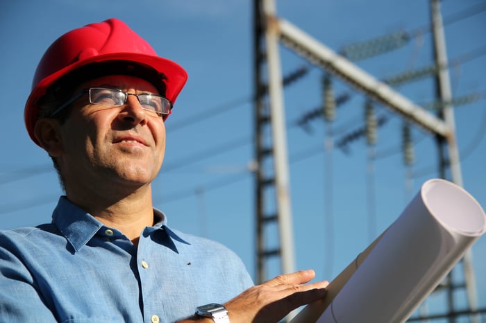 A man with blueprints in his hands with high-voltage power lines behind him