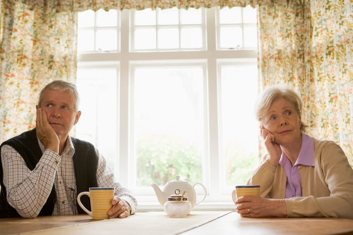 Senior man and woman sitting at a table looking concerned.