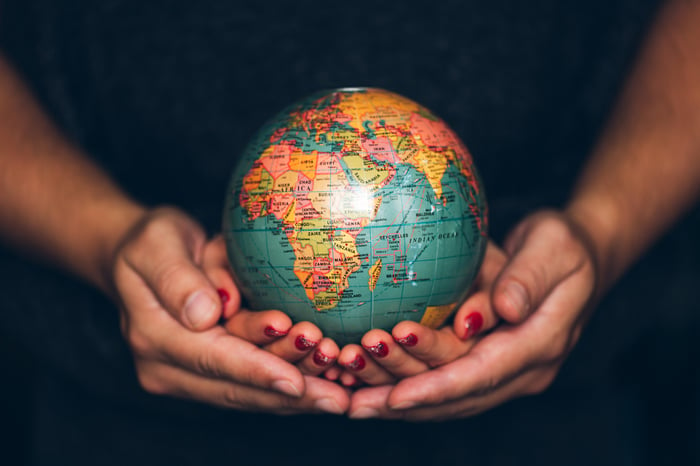 A man and a woman with nested cupped hands holding a globe