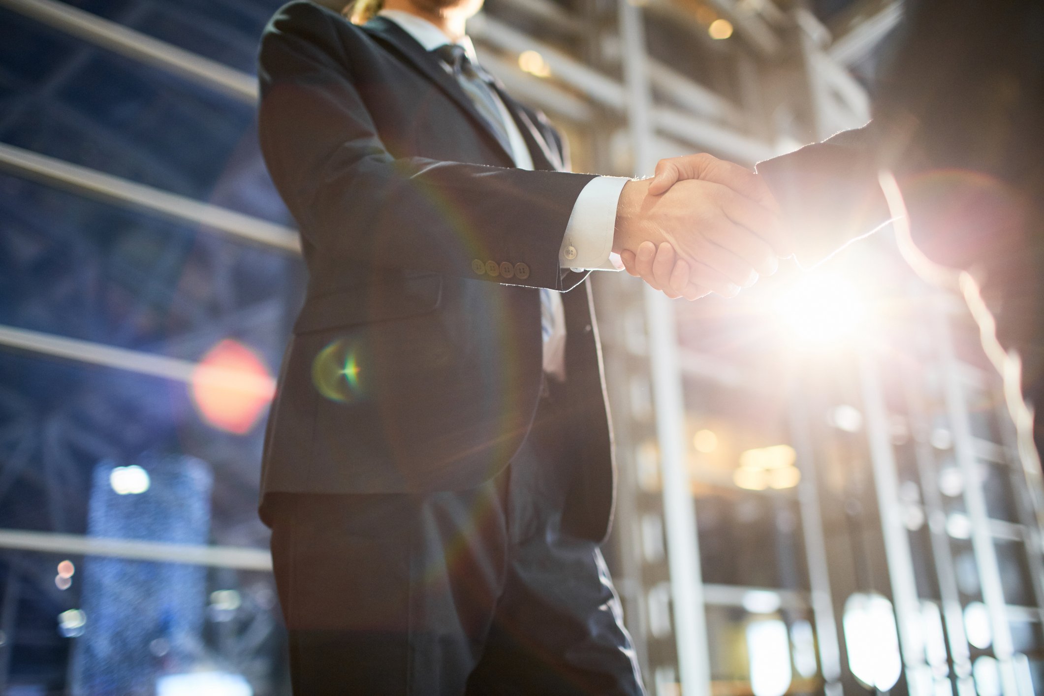 Two people in suits shaking hands in front of a building.