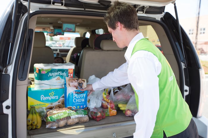 A Walmart worker loading groceries into the back of an SUV.