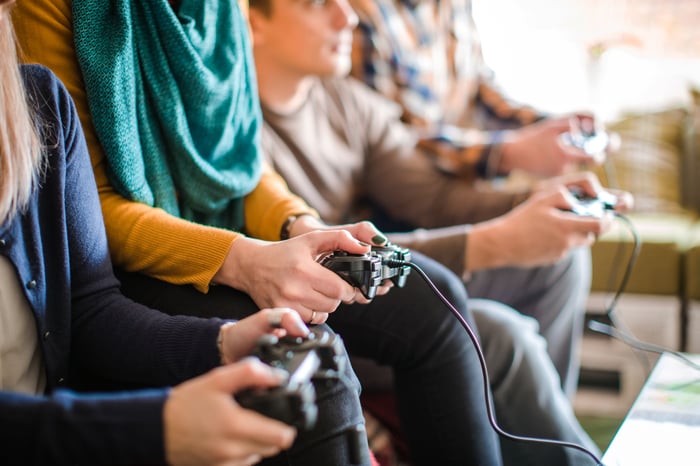 Multiple teens holding video game controllers while seated on a couch.