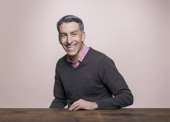 Profile photo of Redfin CEO Glenn Kelman sitting, left hand on a table.