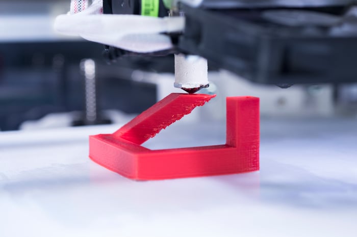 A 3D printer printing an unidentifiable red plastic object.