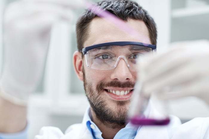 Happy guy with a lab coat, lab glasses, and a pipette.