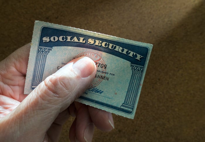 A person tightly gripping a Social Security card between their thumb and index finger. 