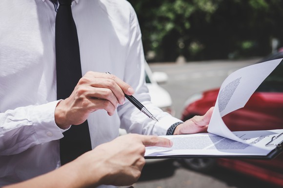 two people reviewing a clipboard of documents with red and white cars in the background