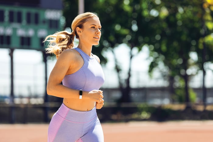 A woman wearing a Fitbit device while jogging.