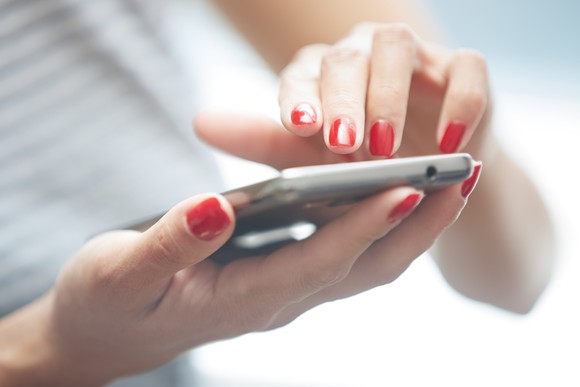 A woman's manicured hands typing on a mobile phone.