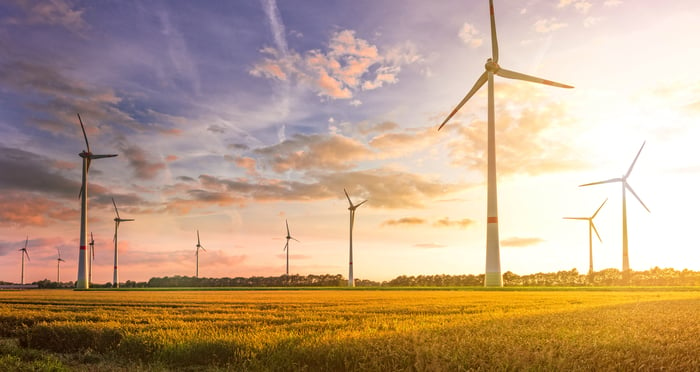 Several wind turbines in a field with a bright sun in the background.