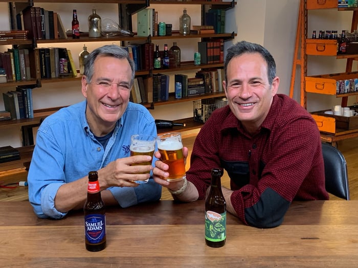 Jim Koch of Boston Beer and Sam Calagione of Dogfish Head sitting at a table and holding their flagship beers.