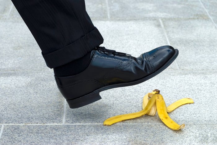 The foot of a man in a black wingtip shoe about to step on a banana peel.