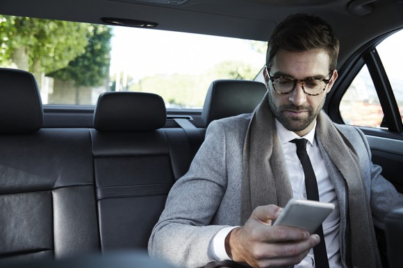 A man in a suit in the back of a car looking at his smartphone.
