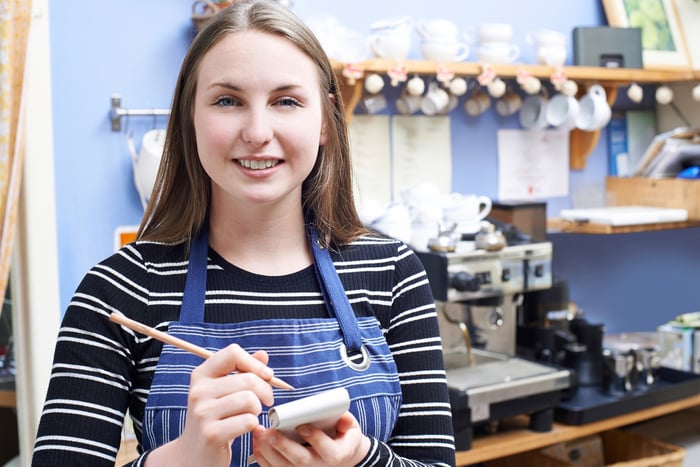 Young female adult in apron taking notes on pad