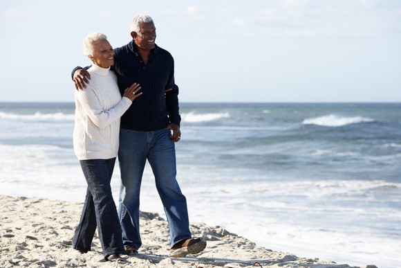 Senior man and senior woman walking on beach with arms around each other