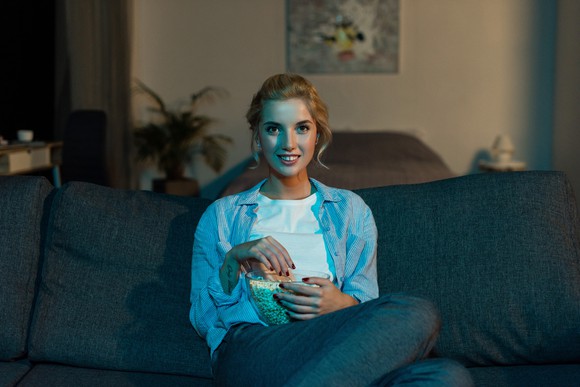 A young woman watching TV while eating popcorn
