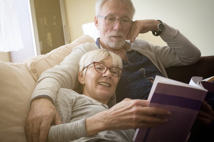 Senior couple on couch, reading a book.