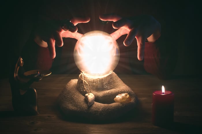 A glowing crystal ball with hands positioned above in a darkened room.