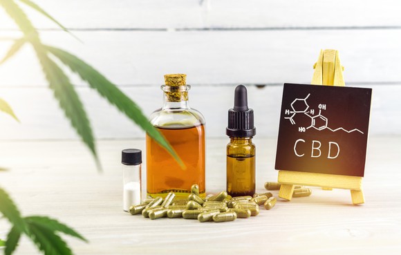 Cannabis leaves, CBD oils, CBD pills, and a small chalkboard with the chemical structure of CBD drawn on it.
