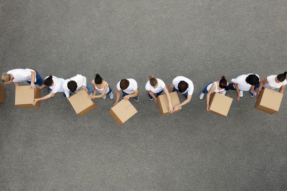A line of individuals passing cardboard boxes from one end to the other.