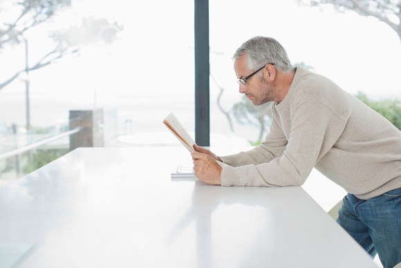 Older man leaning on table while reading newspaper