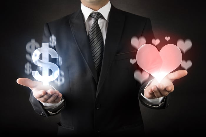 A man in a suit with money symbols in one hand and hearts in the other.