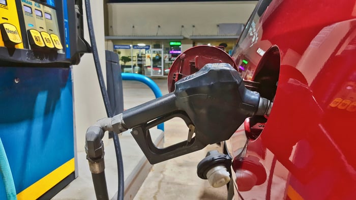 A gas pump filling up a car, with a convenience store in the background.